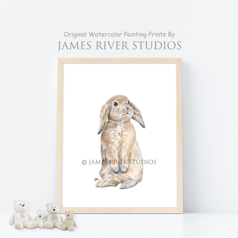 May include: A watercolor painting of a brown lop-eared rabbit standing on its hind legs. The rabbit has a white nose and white markings on its face. The painting is framed in a light wood frame. &copy; JAMES RIVER STUDIOS