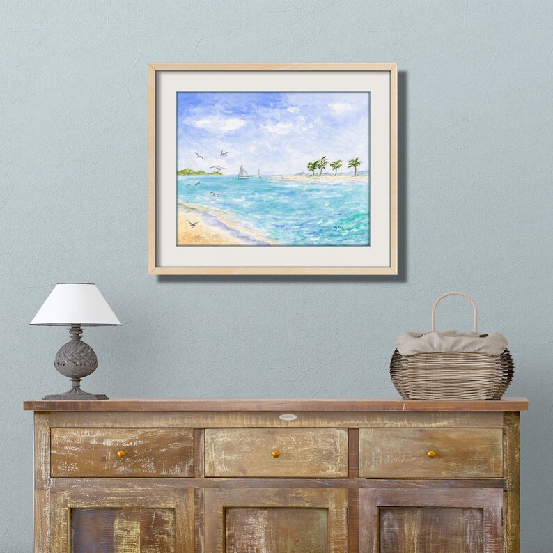 May include: A framed watercolor painting of a seascape with a sailboat in the distance, palm trees on a small island, and a sandy beach. The sky is blue with white clouds.