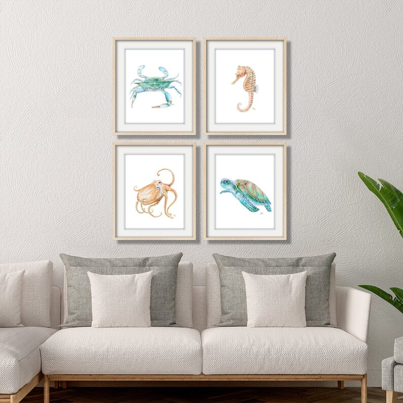 Puede incluir: Conjunto de cuatro impresiones enmarcadas de acuarela con criaturas marinas. Las impresiones representan un cangrejo azul, un caballito de mar, un pulpo y una tortuga marina. Las impresiones est&aacute;n todas en un marco blanco con un acabado de madera clara.