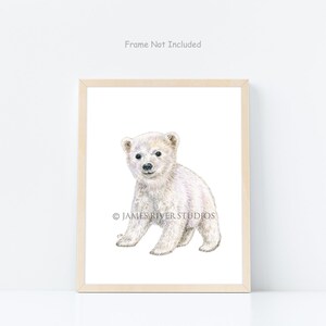 May include: A framed print featuring a watercolor illustration of a polar bear cub. The cub is depicted in white and light grey tones, with a soft, fluffy appearance. The print is in a light wood frame, with the text "Frame Not Included" at the top.