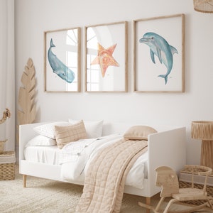 Op de afbeelding: Drie ingelijste aquarel illustraties van zeeleven. De illustraties zijn van een walvis, een zeester en een dolfijn. De lijsten zijn van licht hout en de illustraties zijn op een witte achtergrond.