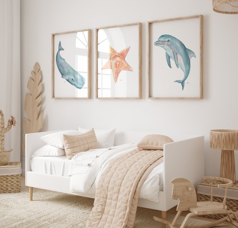 Op de afbeelding: Drie ingelijste aquarel illustraties van zeeleven. De illustraties zijn van een walvis, een zeester en een dolfijn. De lijsten zijn van licht hout en de illustraties zijn op een witte achtergrond.