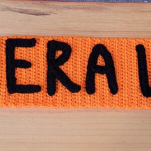 May include: Orange knitted band with the words "GENERAL LEE" in large black letters. A red square with a blue and white design is on the left side. The number "10" is on the right side.