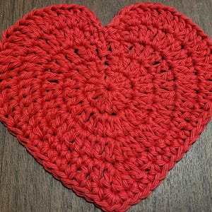 May include: A red crocheted heart-shaped coaster. The coaster is made with a simple stitch pattern and has a slightly textured surface.