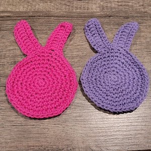 May include: Four crocheted bunny-shaped coasters in blue, pink, purple, and green.