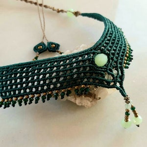 Peut inclure: Un collier ras de cou en macramé vert foncé avec des perles de pierres précieuses vert clair et des accents dorés. Le collier a un design délicat et complexe et est parfait pour ajouter une touche de style bohème à n'importe quelle tenue.