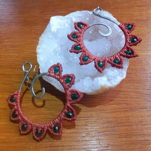 Peut inclure: Une paire de boucles d'oreilles faites à la main avec un design en spirale. Les boucles d'oreilles sont faites de fil rouge et vert et comportent de petites perles vertes.