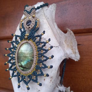 May include: A blue and gold macrame necklace with a large oval labradorite gemstone pendant.