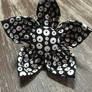May include: A black and white fabric flower with a circle pattern. The flower has five petals and a center button.