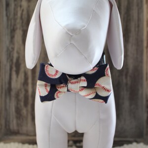 May include: A white dog mannequin wearing a navy blue bow tie with a white baseball pattern.