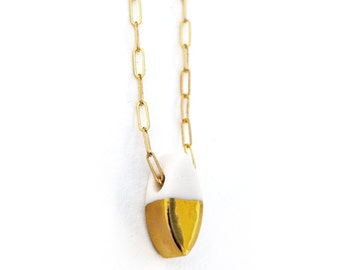 May include: A gold chain necklace with a white ceramic pendant. The pendant is half white and half gold.
