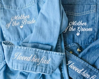 Puede incluir: Dos camisas vaqueras de manga larga con botones. La camisa azul claro tiene bordado en blanco Mother of the Bride e I loved her first. La camisa azul oscuro tiene bordado en blanco Mother of the Groom e I loved him first.