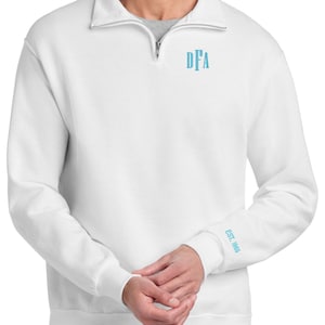 May include: White long-sleeve sweatshirt with a quarter-zip collar. The letters "DFA" are embroidered in light blue on the chest, and "EST. 1986" is on the left sleeve cuff. The sweatshirt is a casual style.