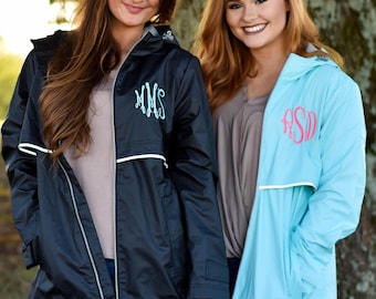 May include: A black hooded rain jacket with a white horizontal stripe and a teal monogram on the chest, alongside a light blue hooded rain jacket with a white horizontal stripe and a pink monogram on the chest, both featuring front zippers.