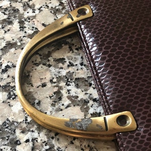 May include: A brown leather handbag with a brass handle. The handle is worn and has a few scratches.
