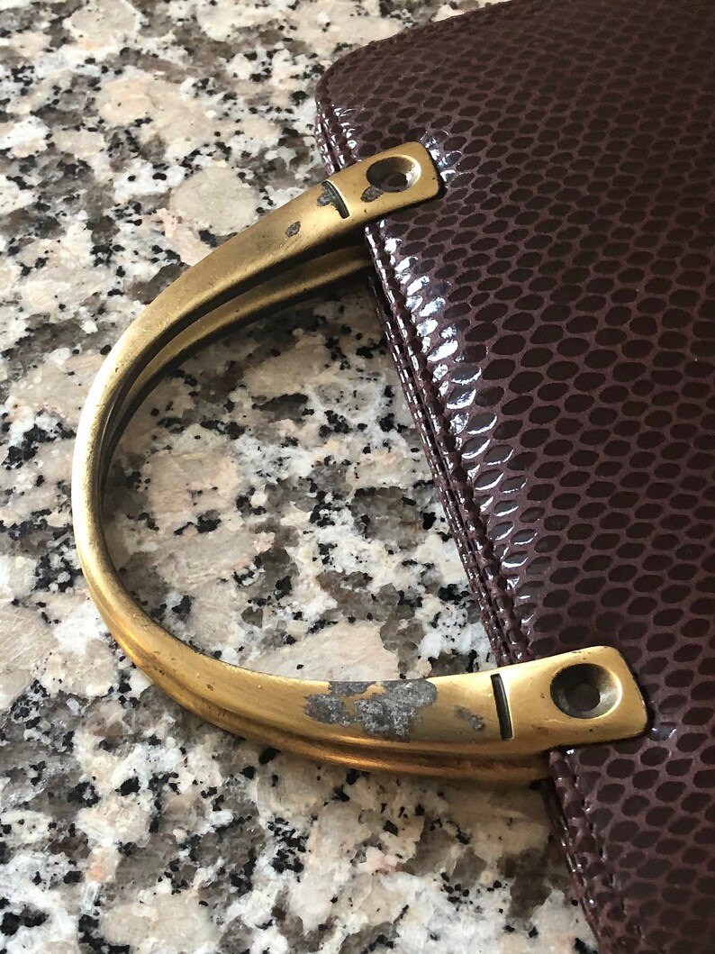 May include: A brown leather handbag with a brass handle. The handle is worn and has a few scratches.