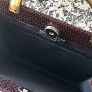May include: A brown snakeskin handbag with a gold metal handle and a black fabric interior. The bag has a zipper closure and a metal clasp.