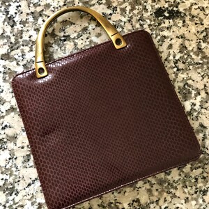 May include: A burgundy leather handbag with a snakeskin pattern and a gold-toned top handle.