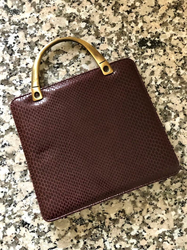 May include: A burgundy leather handbag with a snakeskin pattern and a gold-toned top handle.