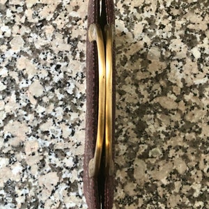 May include: A brown clutch purse with a gold metal clasp and a double-loop handle.