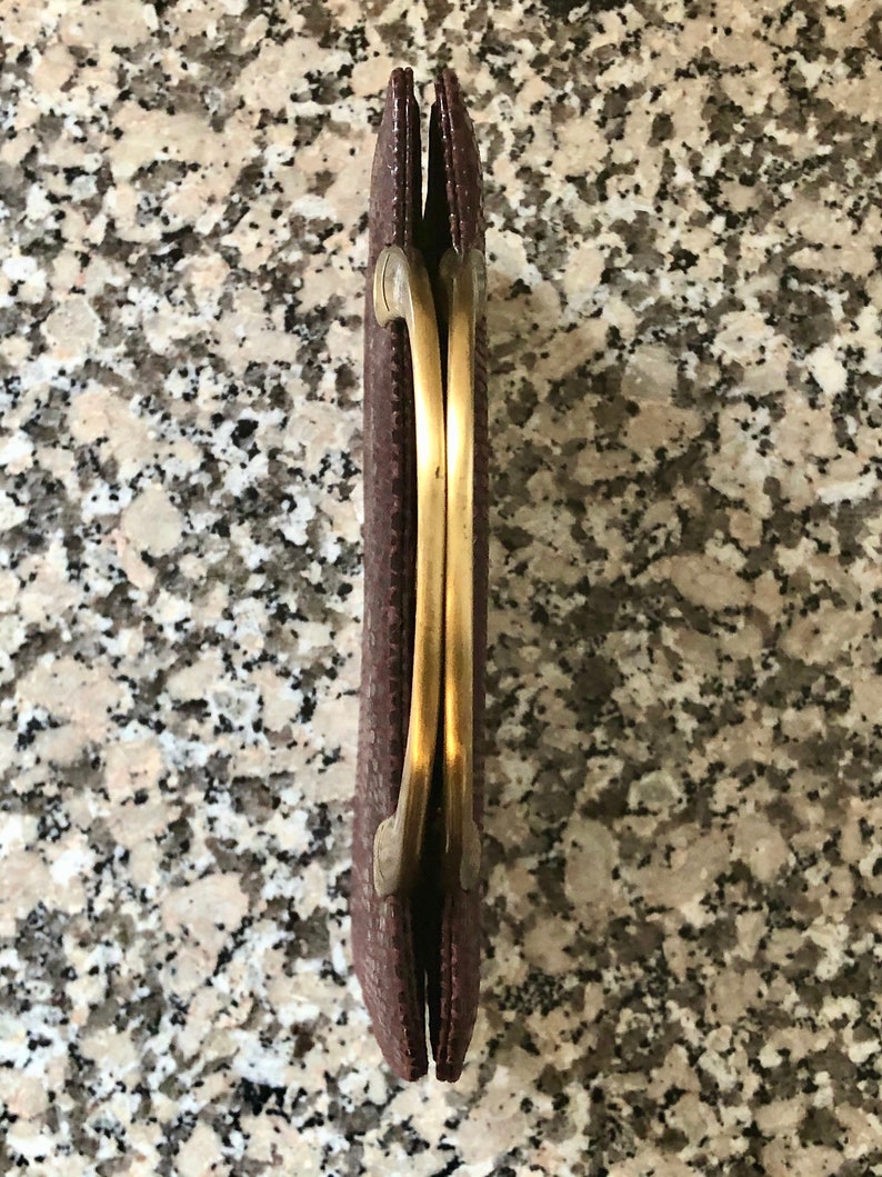 May include: A brown clutch purse with a gold metal clasp and a double-loop handle.