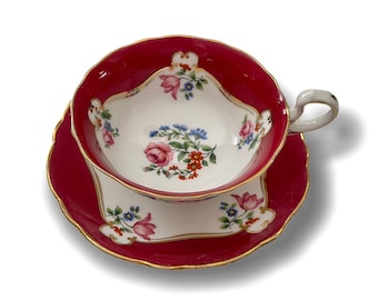 May include: A vintage teacup and saucer set with a red and white floral pattern. The cup has a gold rim and the saucer has a scalloped edge.