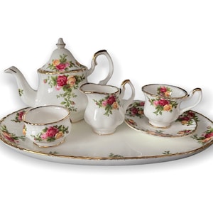 May include: A white porcelain tea set with a floral pattern. The set includes a teapot, creamer, sugar bowl, cup and saucer, and a tray. The floral pattern features red, pink, and yellow roses.