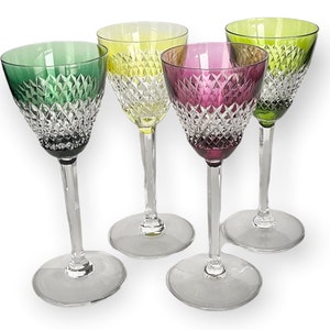 May include: Four colorful wine glasses with diamond-cut patterns. The glasses have clear stems and bases, with bowls in green, yellow, purple, and another shade of green. The glasses are arranged on a white background.