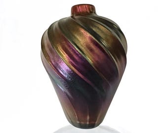 May include: A decorative iridescent glass vase with a spiral design. The vase has a teardrop shape and a small neck. The colors shift from gold to purple and dark green. The vase is approximately 8 inches tall.