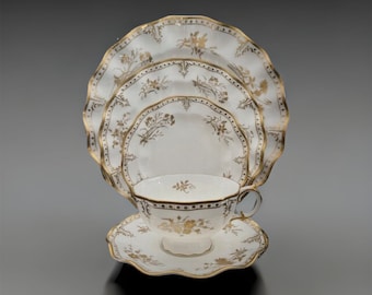 May include: A set of white porcelain teacups and saucers with a delicate floral pattern in gold. The set includes a teacup, saucer, and two larger plates.