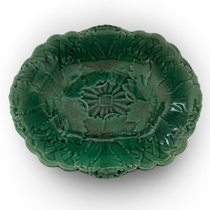Puede incluir: Una fuente ovalada de cerámica verde con un diseño detallado de hojas y flores. La fuente tiene un borde festoneado y un motivo floral central en relieve. El color verde oscuro y los intrincados detalles le dan una estética vintage.