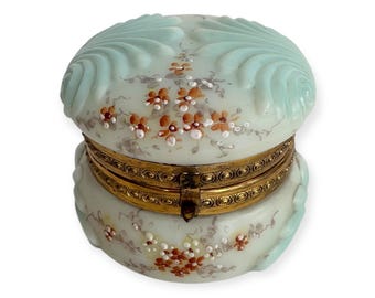 May include: A vintage, two-piece, round, hinged trinket box with a pale blue and white floral design. The box is decorated with a raised, scalloped pattern and has a gold-toned hinge and clasp.