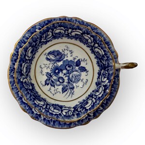 May include: A blue and white porcelain teacup and saucer with a floral design. The cup and saucer have a gold trim.