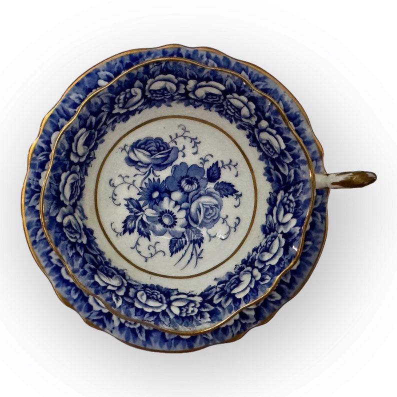 May include: A blue and white porcelain teacup and saucer with a floral design. The cup and saucer have a gold trim.