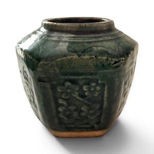 May include: A dark green ceramic jar with an octagonal body and a narrow neck. The jar has embossed floral patterns and a slightly rough texture. The base is light brown.