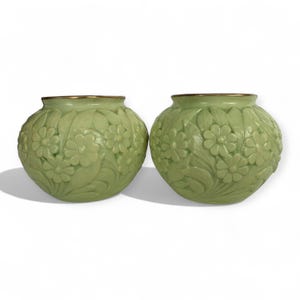Puede incluir: Dos jarrones de cerámica verde a juego con un diseño floral. Los jarrones tienen forma redonda y un borde dorado. El patrón floral está en relieve en la superficie, creando un efecto texturizado. Los jarrones se muestran sobre un fondo blanco.