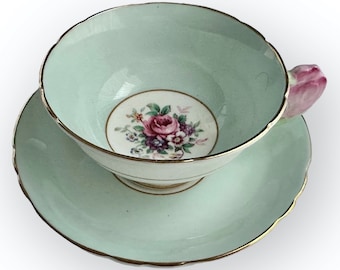 May include: A light blue teacup and saucer set with a floral design. The teacup has a unique handle shaped like a rose bud.