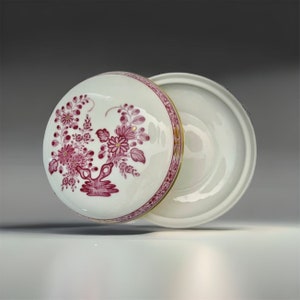 May include: A white porcelain lidded box with a pink floral design and gold trim. The lid is open and the box is sitting on a white surface.