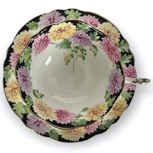 May include: A vintage teacup and saucer set with a black background and a floral design featuring pink, yellow, and white chrysanthemums.