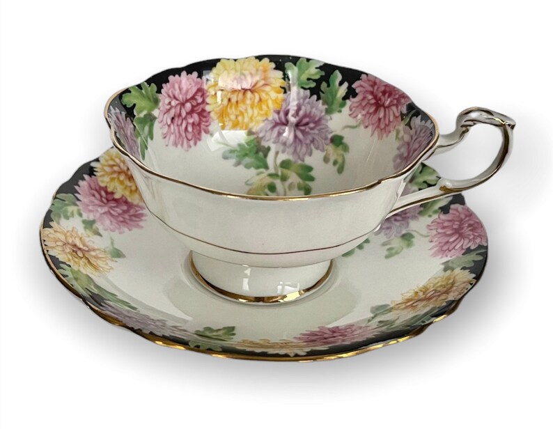 May include: A white teacup and saucer with a black rim and a floral pattern of pink, yellow, and purple chrysanthemums.