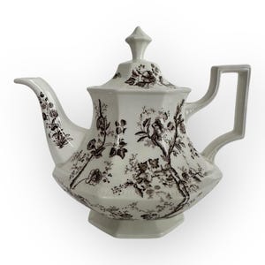 以下が含まれることがあります： 茶色の花柄が施された白いティーポット。ティーポットは、つまみ付きの蓋と取っ手があります。
