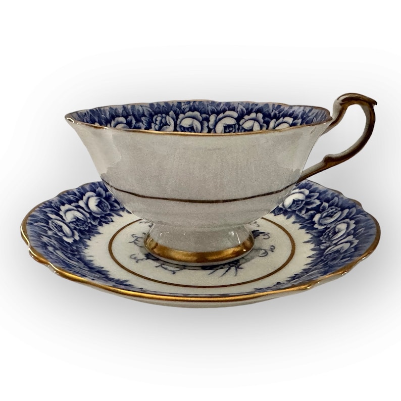 May include: A white teacup and saucer with a blue and gold floral pattern. The cup has a scalloped rim and a delicate handle. The saucer has a matching scalloped edge.