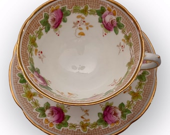 Puede incluir: Una taza de té y un platillo blancos con un borde dorado y un patrón floral. El patrón presenta rosas rosadas, hojas verdes y enredaderas marrones sobre un fondo blanco.