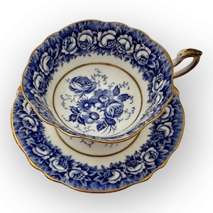 May include: A blue and white teacup and saucer set with a floral design. The cup and saucer have a gold trim.