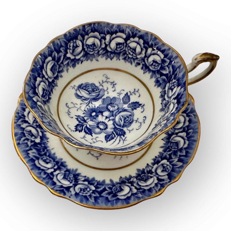 May include: A blue and white teacup and saucer set with a floral design. The cup and saucer have a gold trim.