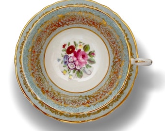 May include: A vintage teacup and saucer with a delicate floral design in shades of pink, purple, and green. The cup and saucer are trimmed with gold accents and have a light blue background.