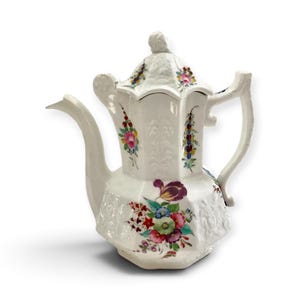 Könnte beinhalten: Eine weiße Porzellanteekanne mit achteckigem Körper und passendem Deckel. Die Oberfläche ist mit Reliefmustern und handgemalten Blumenmotiven in Rosa, Violett, Blau, Gelb und Grün verziert. Sie verfügt über einen geschwungenen Ausguss und Henkel.