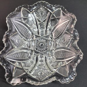 May include: Clear glass serving bowl with a starburst and geometric pattern. The bowl has a scalloped edge and a detailed design, ideal for serving snacks or displaying decorative items.