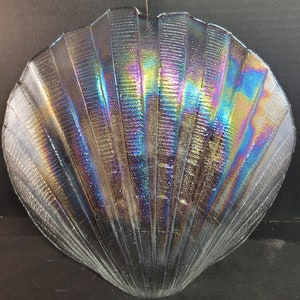 May include: A iridescent glass seashell dish with a textured surface. The dish is shaped like a scallop shell and has a light blue, purple, and green iridescent finish.