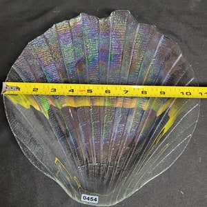 May include: A clear glass iridescent seashell-shaped dish with a textured surface. The dish is approximately 10 inches wide. The number 0454 is written on the bottom of the dish.